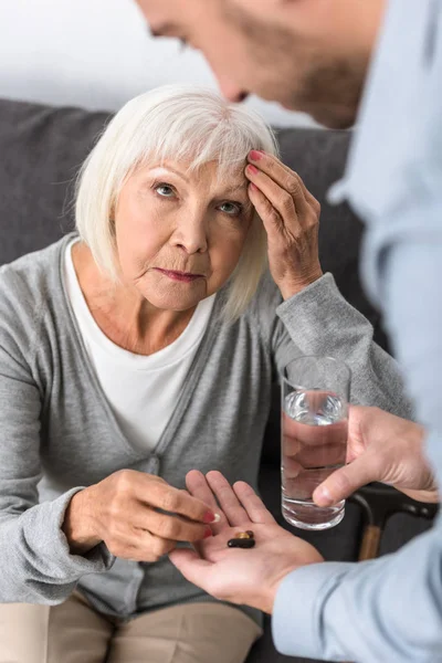 Cropped view of man giving to senior mother glass of water and medicine — Stock Photo