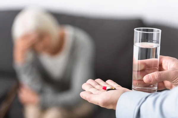 Vista recortada del hombre dando a la madre mayor vaso de agua y medicina - foto de stock