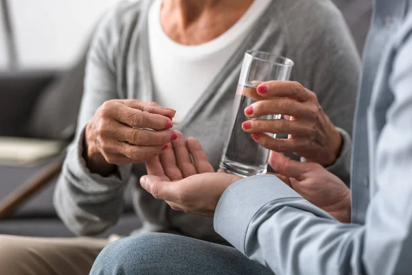 Vista recortada del hombre dando a la madre mayor vaso de agua y medicina - foto de stock