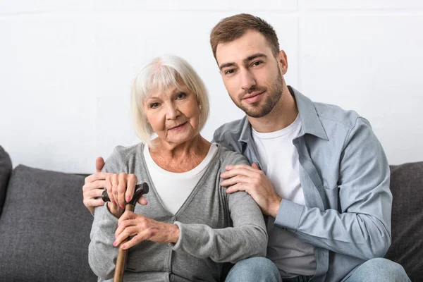 Mann sitzt auf Sofa und umarmt Seniorin im Wohnzimmer — Stockfoto