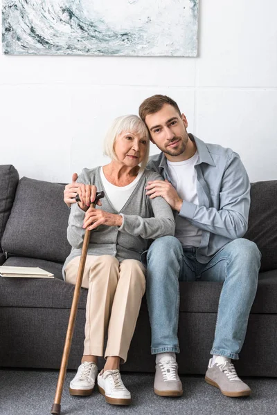 Mann sitzt auf Sofa und umarmt Seniorin — Stockfoto