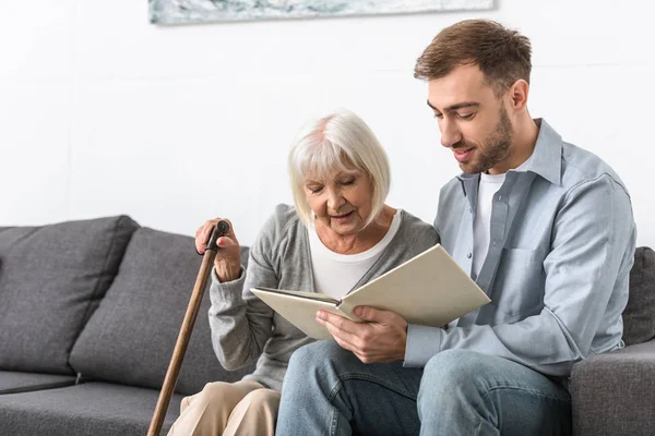 Man sitting on sofa and reading book with senior mother — Stock Photo