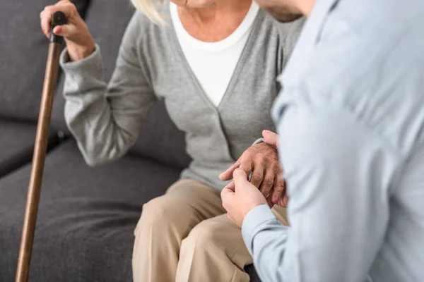 Vue partielle de l'homme tenant la main avec sa mère aînée — Photo de stock