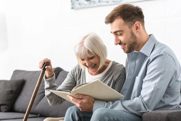 Mann sitzt mit älterer Mutter auf Sofa und liest Buch — Stockfoto