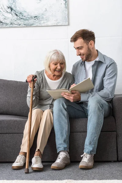 Mann sitzt mit älterer Mutter auf Sofa und liest Buch — Stockfoto