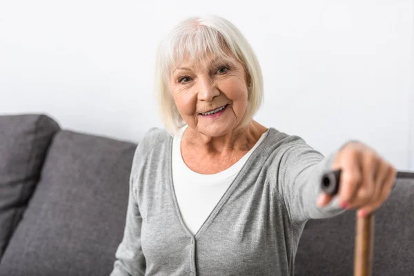 Sonriente mujer mayor con bastón de madera mirando a la cámara - foto de stock