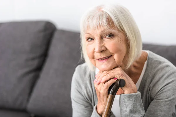 Femme âgée souriante avec canne en bois regardant la caméra — Photo de stock