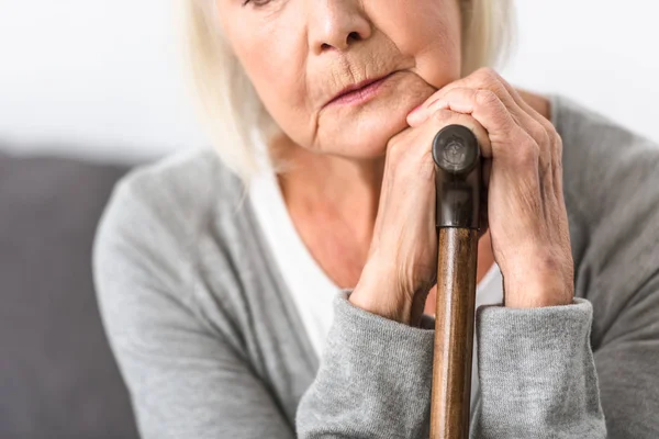 Cropped view of pensive senior woman with wooden cane — Stock Photo