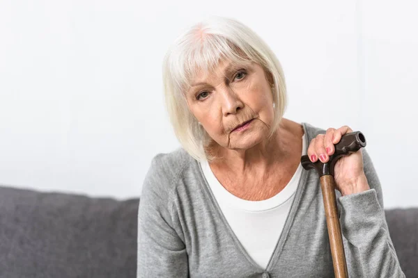 Nachdenkliche Seniorin mit Holzstock blickt in Kamera — Stockfoto