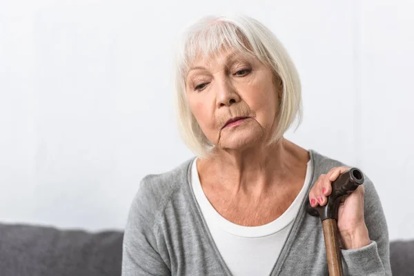 Pensive senior woman with wooden cane looking down — Stock Photo