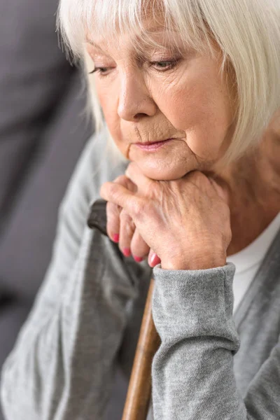 Pensive senior woman holding wooden cane and looking down — Stock Photo