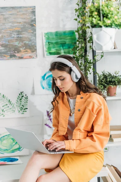 Attentive girl in headphones using laptop while sitting on desk at home — Stock Photo