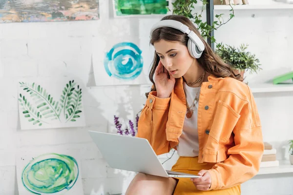 Menina bonita atenciosa usando laptop enquanto ouve música em fones de ouvido — Fotografia de Stock
