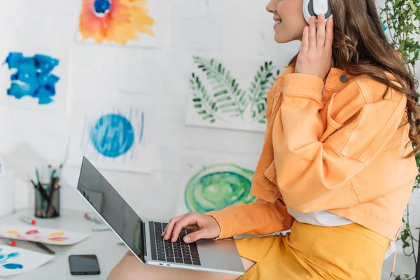 Vista parziale di giovane donna che ascolta musica in cuffia e utilizzando il computer portatile — Foto stock