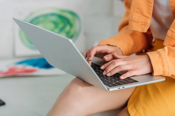 Partial view of young woman in orange clothing using laptop at home — Stock Photo