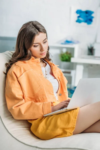 Réfléchie jeune femme en orange fermeture à l'aide d'un ordinateur portable à la maison — Photo de stock