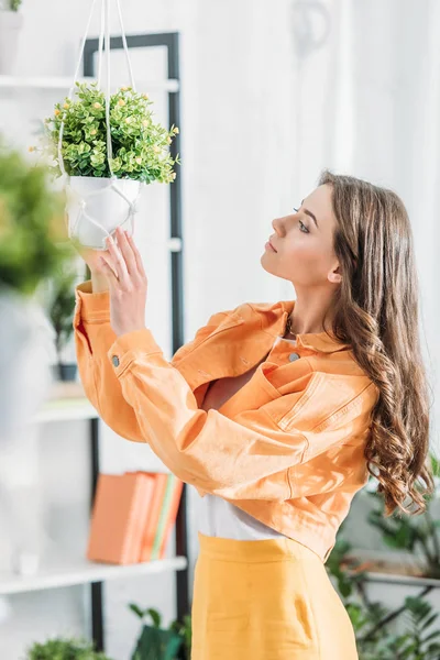 Selective focus of pensive beautiful woman in orange clothing  touching flowerpot — Stock Photo