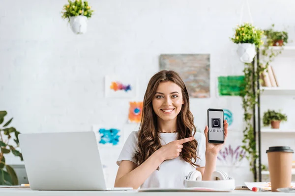 KYIV, UKRAINE - 17 AVRIL 2019 : Jolie jeune femme pointant du doigt son smartphone avec l'application Uber à l'écran . — Photo de stock