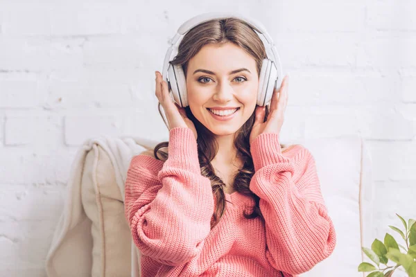 Beautiful young woman listening music in headphones and looking at camera — Stock Photo