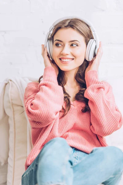 Joyeuse jeune femme écoutant de la musique dans les écouteurs et détournant les yeux — Photo de stock