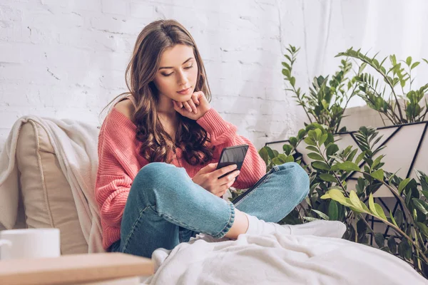 Thoughtful young girl using smartphone while sitting with crossed legs — Stock Photo