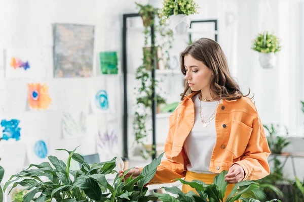 Belle jeune fille touchant les plantes vertes luxuriantes dans une chambre spacieuse — Photo de stock