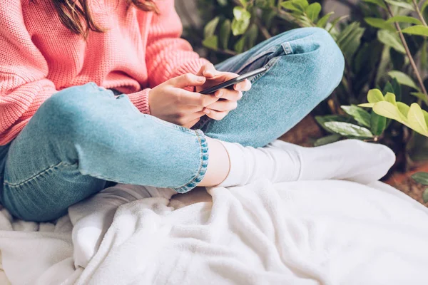 Cropped view of girl sitting with crossed legs and using smartphone — Stock Photo