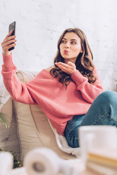 Foco seletivo de menina alegre enviando beijo de ar ao ter bate-papo de vídeo no smartphone — Fotografia de Stock