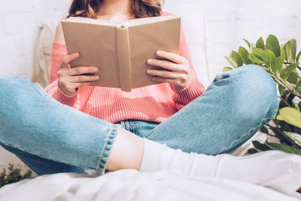 Vista parcial de la joven sentada con las piernas cruzadas y el libro de lectura - foto de stock