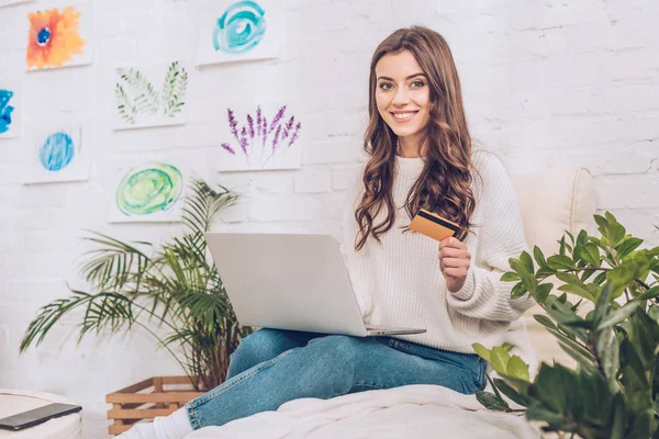 Happy girl using smartphone and holding credit card while smiling at camera — Stock Photo