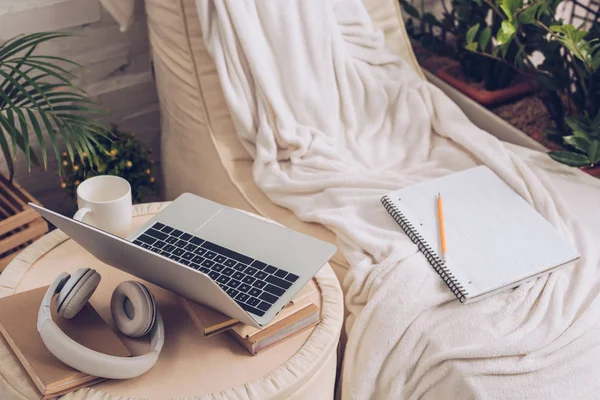 Laptop, fones de ouvido, livros e xícara de café no pufe perto do salão de chaise macio — Fotografia de Stock