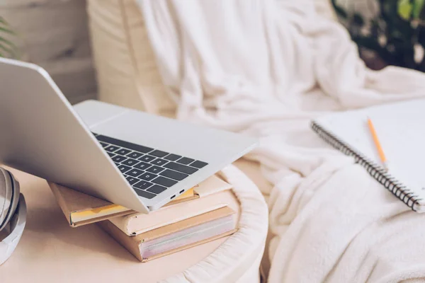 Selective focus of laptop and books near soft white chaise lounge covered with white blanket — Stock Photo