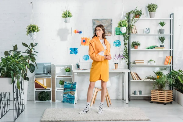 Mulher elegante em pé no centro de quarto espaçoso decorado com plantas verdes e pinturas na parede branca — Fotografia de Stock