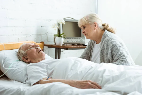 Sad senior woman with husband in coma in hospital — Stock Photo