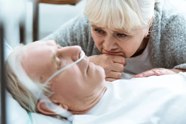 Sad senior woman with husband in coma in clinic — Stock Photo