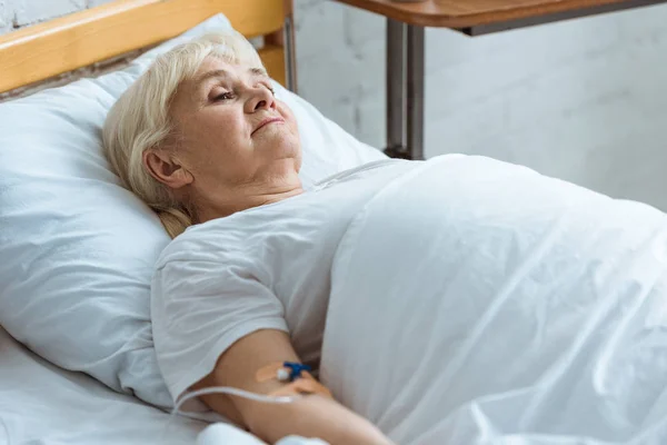 Sick senior woman with grey hair on bed in clinic — Stock Photo