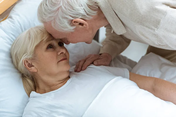 Sick senior woman with husband looking at each other in ward in clinic — Stock Photo