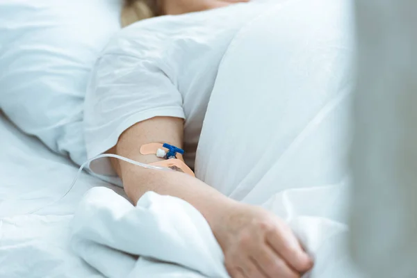 Visión parcial de la mujer enferma acostada en la cama durante la terapia intravenosa en la clínica - foto de stock