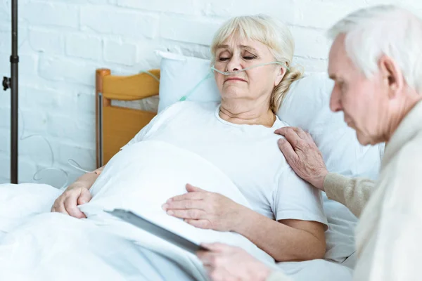 Senior man holding clipboard with sick wife in clinic — Stock Photo