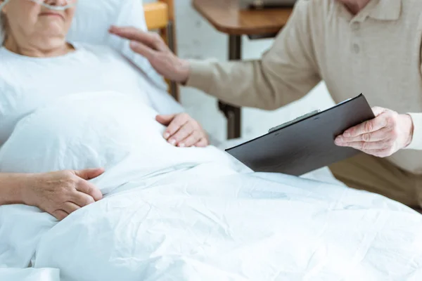 Обрезанный вид пожилого человека, держащего планшет с больной женой в клинике — стоковое фото