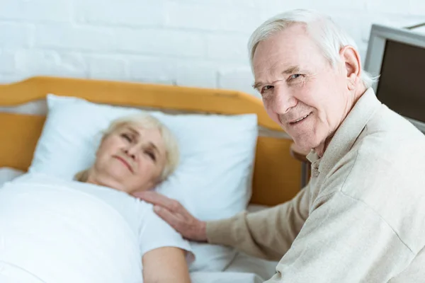 Sonriendo hombre mayor con esposa enferma en la clínica - foto de stock