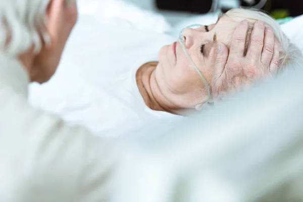 Visão cortada de homem sênior acariciando esposa em coma na clínica — Fotografia de Stock