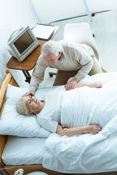 Overhead view of senior man stroking wife in coma in clinic — Stock Photo