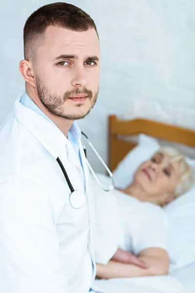 Médecin en manteau blanc et malade aîné couché sur le lit — Photo de stock