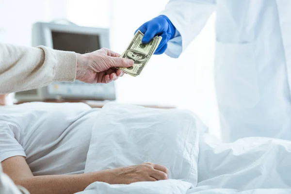 Partial view of sick patient and senior man giving bribe to doctor — Stock Photo
