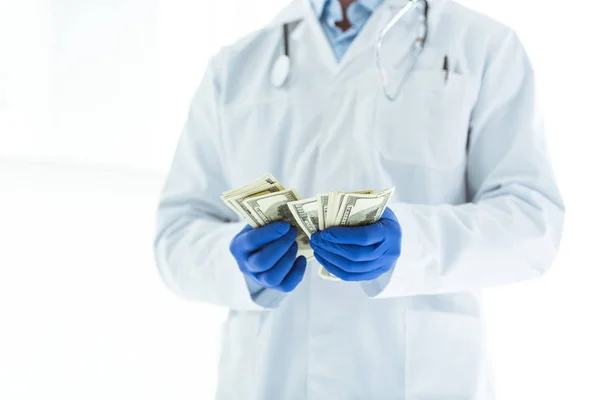 Partial view of doctor in latex gloves counting dollar banknotes on white — Stock Photo