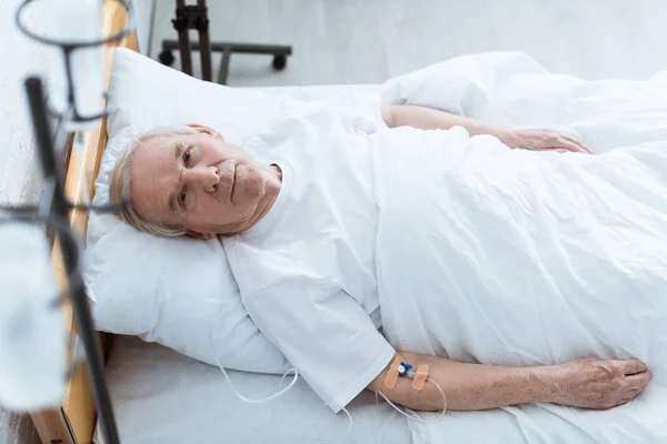 Overhead view of sick senior man lying on bed in clinic — Stock Photo