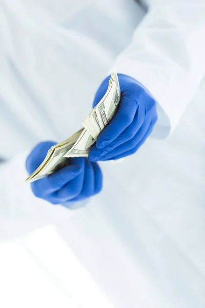 Частичный взгляд врача в латексных перчатках, считая долларовые купюры на белом — стоковое фото