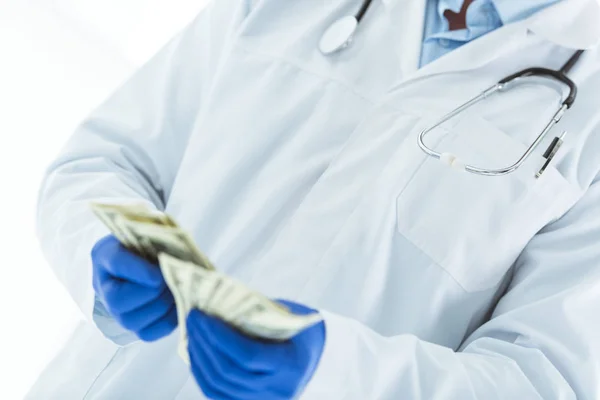 Partial view of doctor in latex gloves counting dollar banknotes on white — Stock Photo