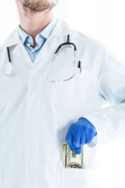 Partial view of doctor in white coat putting dollar banknotes in pocket isolated on white — Stock Photo